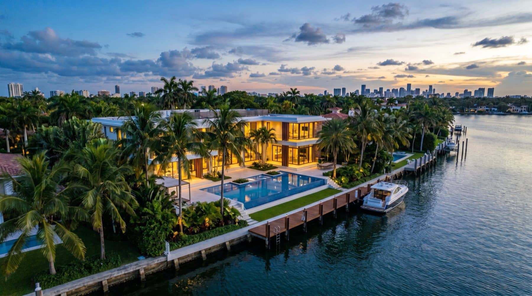 Twilight aerial of a luxury waterfront Miami home with a pool, dock and palm trees, South Florida.